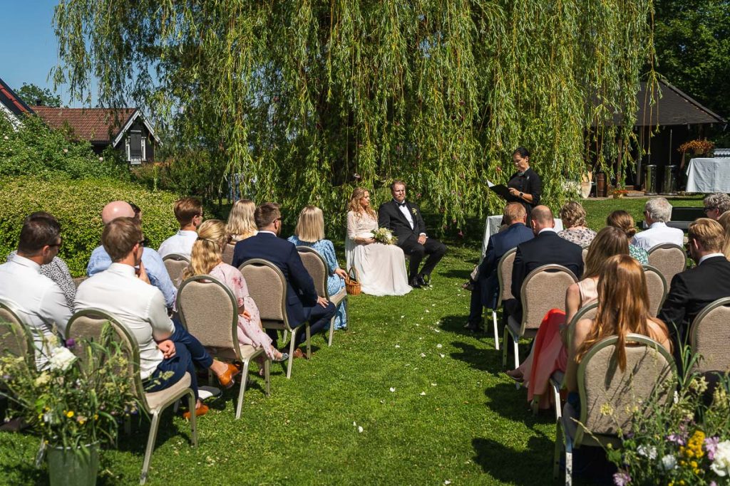 Vigselförrättaren genomför vigseln i trädgården tillsammans med brudpar och bröllopsgäster.