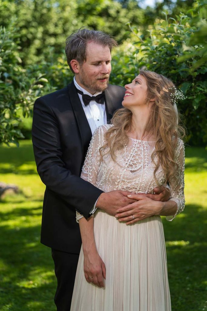Porträtt av brudparet i trädgården omgiven av fruktträd.