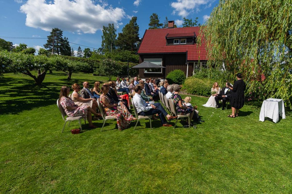 Vigselförrättaren genomför vigseln i trädgården tillsammans med brudpar och bröllopsgäster.