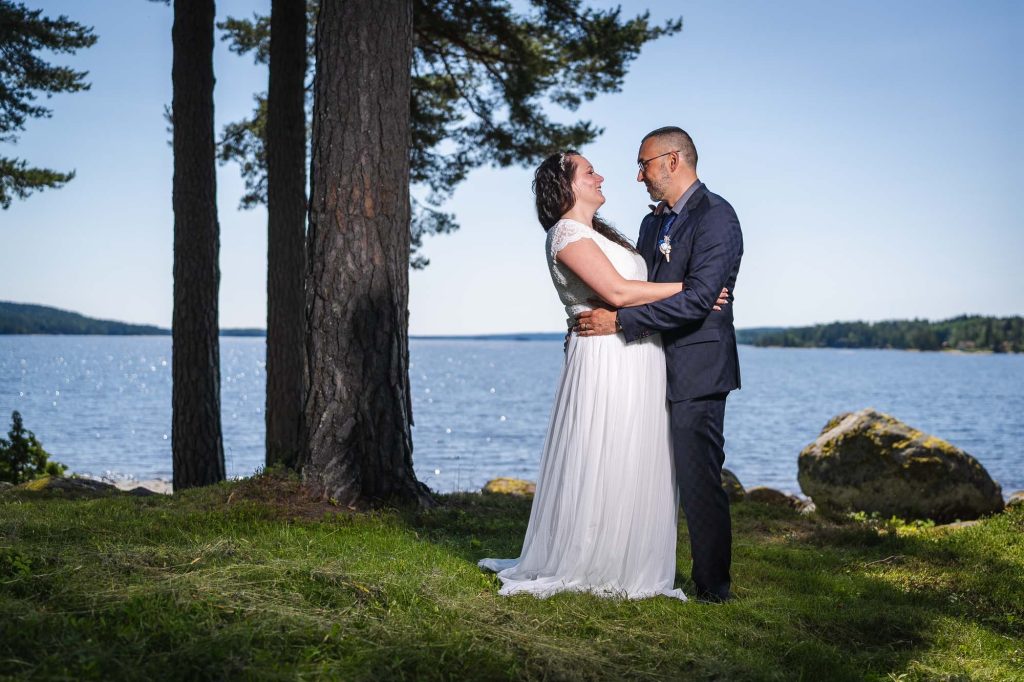 Brudparet står vid sjön Foxen utanför västra Fågelviks kyrka.