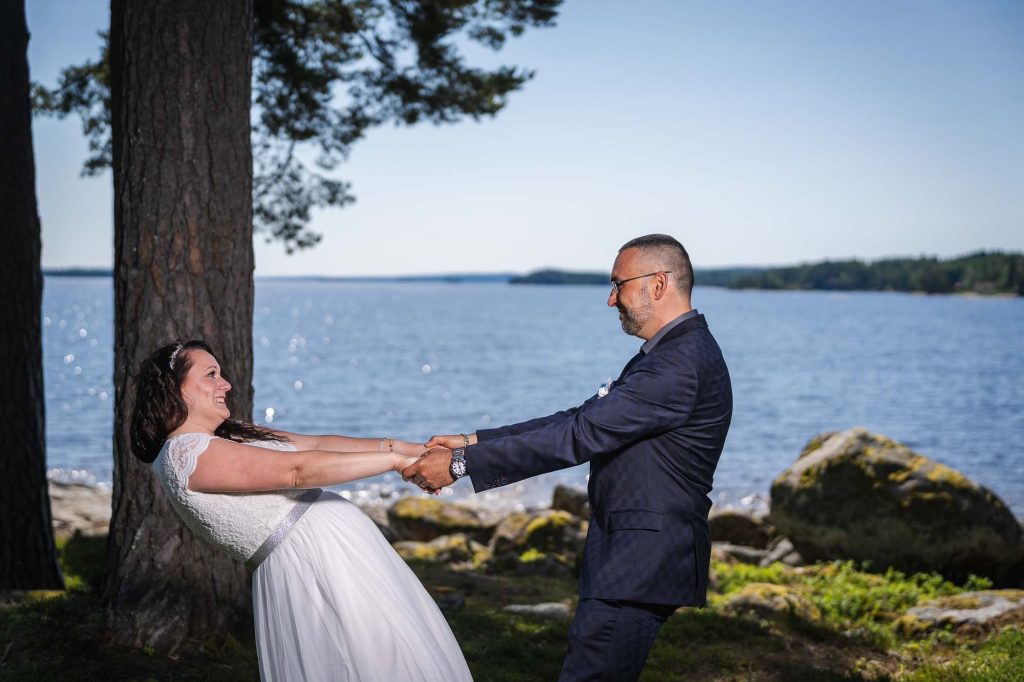 Brudparet står vid sjön Foxen utanför västra Fågelviks kyrka.