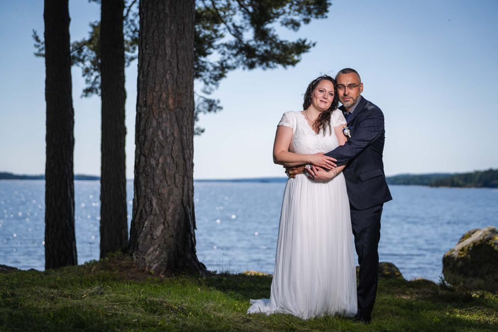 Brudparet står vid sjön Foxen utanför västra Fågelviks kyrka.