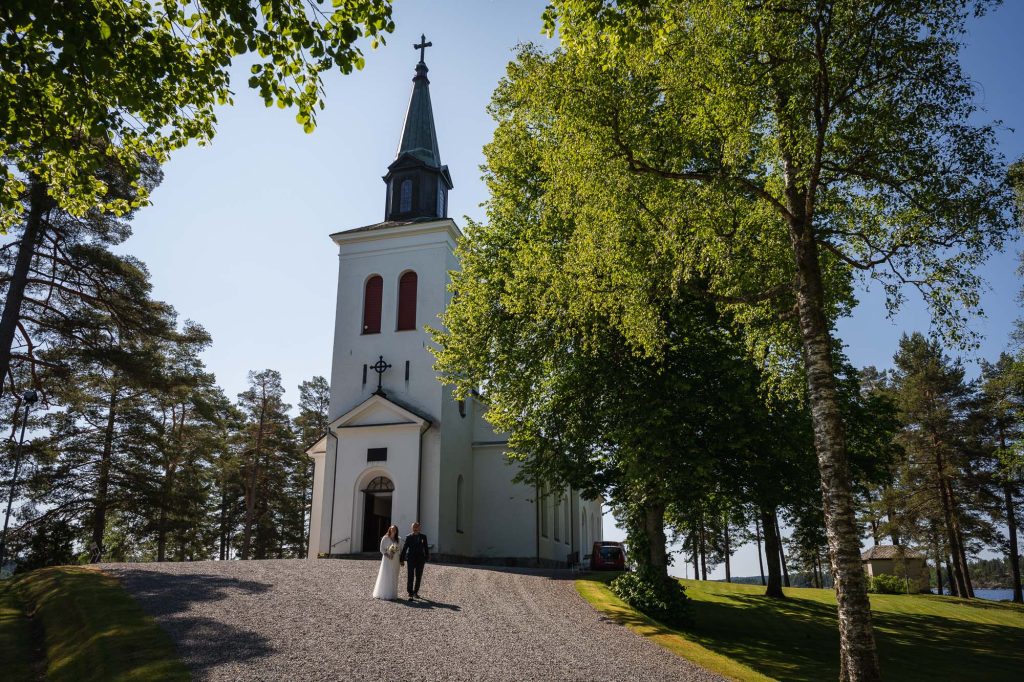 Bröllopsparet går hand i hand före bröllopet framför västra Fågelviks kyrka i Töcksfors.
